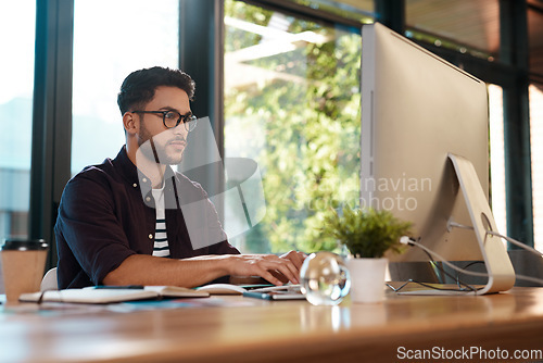 Image of Computer, serious and a business man typing and working at desk while online for research or creative work. Male entrepreneur person with glasses for reading or writing email with internet connection