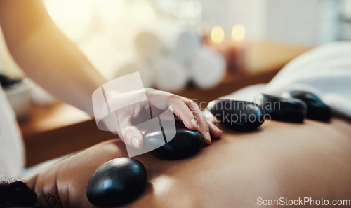 Image of Woman, hands and rocks in relax for back massage, skincare or beauty relaxation on bed at spa. Hand of masseuse applying hot rock or stones on female for physical therapy or treatment at a resort