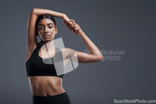 Image of Portrait, mockup and stretch with a sporty woman in studio on a gray background for fitness or health. Exercise, workout and warm up with a young focused indian female athlete training her body