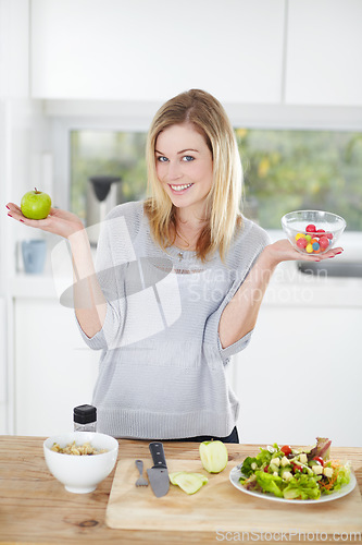 Image of Choice, sweets and woman decide on healthy food in a kitchen for a diet and holding an apple and candy in home. Portrait, smile an happy female person with fruit for nutrition as lunch meal