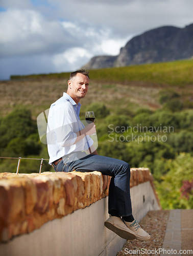 Image of Portrait, mature man with red wine and in vineyard or farm sitting on wall. Agriculture, beverages or drinks with glass and happy male sommelier or farmer with champagne or alcohol outdoors