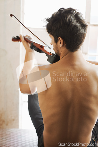 Image of Back, music and a man playing the violin in his home while sitting shirtless as an artist or musician. Body, talent and instrument with a topless male violinist in rehearsal for a theatre performance