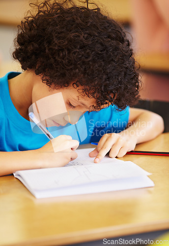 Image of Boy kid, school and writing test in classroom with focus, concentration or thinking for education goals. Male child, book and pen in class for assessment, studying or learning at desk for development