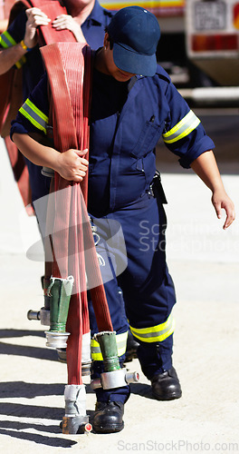 Image of Firefighter, team and carrying hoses for emergency, rescue or fire drill from truck outdoors. Firefighters working together in practice lifting big liquid pressure pipes outside station or department