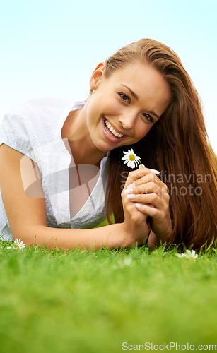 Image of Portrait, happy and woman with daisy on grass, lying down on field and enjoying spring on vacation outdoor. Smile, flower plant and beauty of female person relaxing, mockup and having fun in nature.