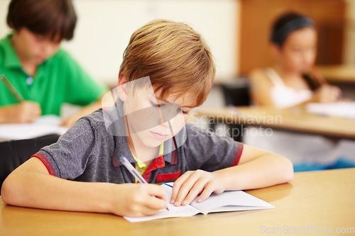 Image of Boy kid, school classroom and writing test with focus, concentration and thinking for education goals. Male child, book and pen in class for assessment, studying or learning at desk for scholarship