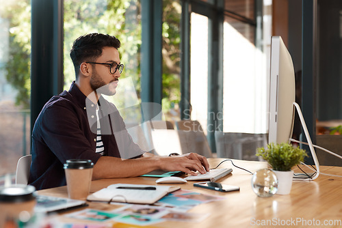 Image of Designer, man and typing online on computer while working at desk for research or creative work. Male entrepreneur person with glasses and focus for reading or writing email with internet connection