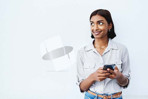 Image of Social media, young Indian woman on smartphone and thinking in studio background. Smiling or idea, phone for communication or networking and happy female person standing with cellphone in backdrop