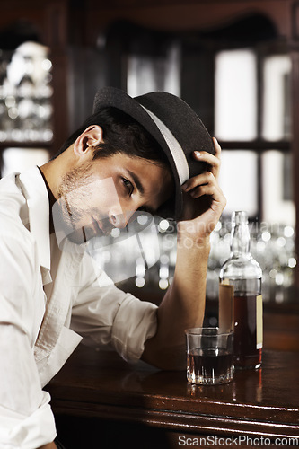 Image of Portrait, whisky and a man sitting at the bar drinking alcohol in a glass while alone or feeling unhappy. Brandy, drink and beverage with a handsome young male pub customer at a wooden counter
