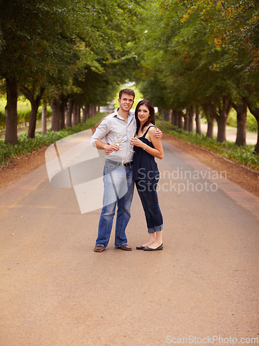 Image of Couple, portrait and wine outdoor at a vineyard for vacation, holiday or travel with love and care. Man and a woman hug on a countryside road with trees, alcohol glass or drinks to celebrate marriage