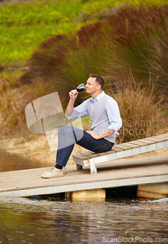 Image of Thinking, river and a man drinking wine outdoor in nature on his farm for agriculture or sustainability. Water, glass and idea with a male person sitting on the pier to drink alcohol alone outside