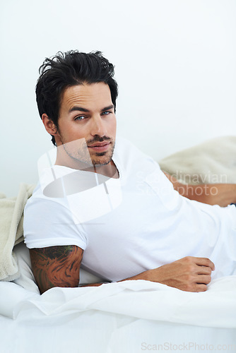 Image of Portrait, relax and bed with a sexy man in the morning on a white background looking casual after wake up. Fashion and confidence with a handsome young male model lying in the bedroom of his home
