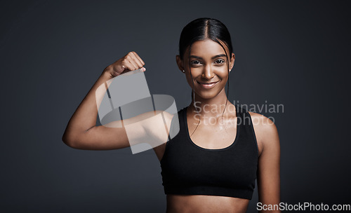 Image of Portrait, smile and woman flexing muscle in studio isolated on black background. Strong, happy and Indian female athlete with bicep, arm strength and bodybuilder workout, fitness or sports exercise.