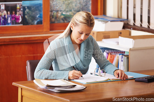 Image of Teacher, education career and a woman writing or marking test paper with a pen at a desk in a classroom. Professional female person working at a academic school with paperwork for exam results