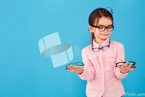Image of Happy, decision and a girl with optometry glasses isolated on a blue background in studio. Smile, young and a little child with eyewear choice for vision, eyesight and choosing spectacles with mockup