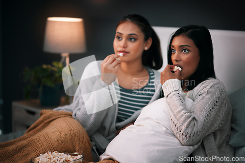 Image of Popcorn, eating and women or friends with horror movies, scary show and sleepover on bed, streaming service or television. Gen z people relax in bedroom for drama TV film, home cinema or subscription