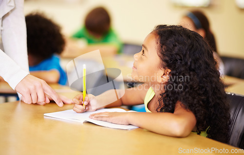 Image of School, education and kids with a student girl in a classroom, writing while talking to her teacher. Children, learning and study with an adorable female kid at a desk in class for child development