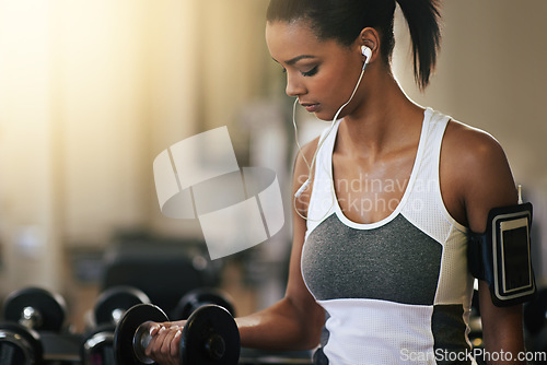 Image of Fitness, music and dumbbell with a woman in the gym, streaming audio through earphones while training. Exercise, workout and weightlifting with a female bodybuilder in a sports club for health