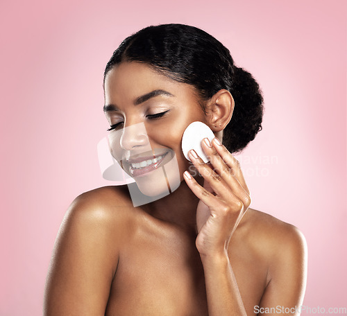 Image of Skincare, mockup and happy woman with cotton pad on face, smile and makeup removal with skin product in studio. Dermatology, facial cleansing cosmetics and African model isolated on pink background.