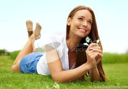 Image of Thinking, smile and woman with daisy on grass, lying down on field and enjoying spring on vacation outdoor. Happy, flower plant and beauty of female person relaxing, smiling and having fun in nature.