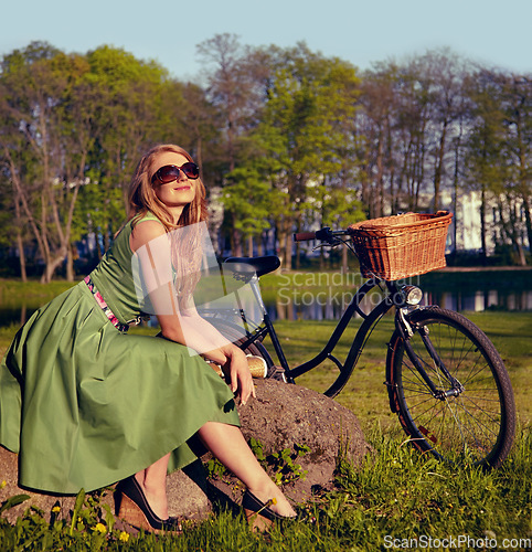 Image of Happy, smile and bicycle with woman in park for cycling, freedom and nature. Spring, relax and peace with female person and bike resting on rock in grass field for health, summer break and happiness