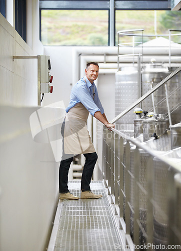 Image of Industry, confidence and portrait of a wine maker standing by stainless steel machines in factory. Proud, smile and full length of a male winery employee doing alcohol production in cellar warehouse.
