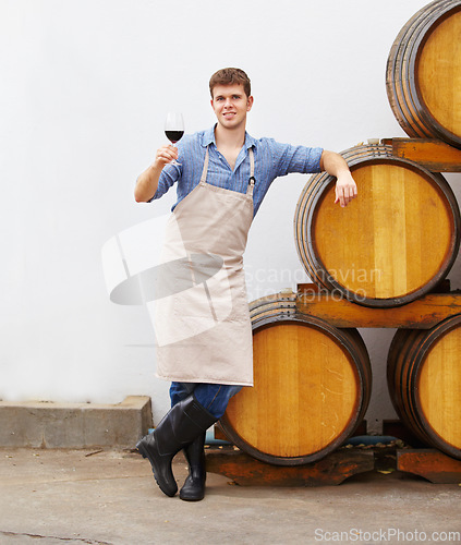 Image of Portrait, wine and oak barrels with a man holding a glass in a winery or distillery as an artisan and sommelier. Drink, red blend and alcohol with a male beverage maker in a factory or warehouse