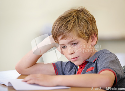 Image of School, education and a boy reading a book at his desk in a classroom for studying or child development. Kids, learning and bored with a young male student child in class to study for an exam or test