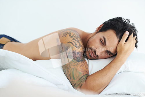 Image of Thinking, relax and shirtless with a sexy man lying on a bed in studio on a white background. Tattoo, idea and topless with a handsome young male model posing in a bedroom for sensuality or desire