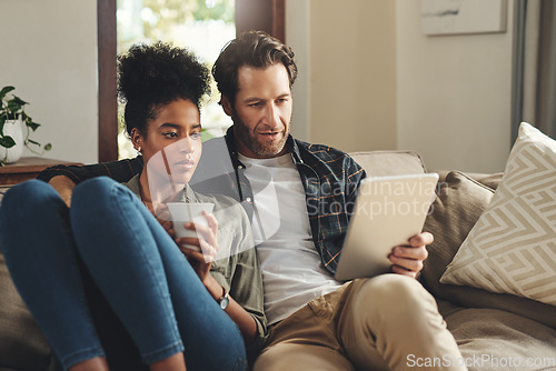 Image of Love, home and couple with a tablet, connection and social media for communication, romance and relax. Partners, man and woman on a couch, interracial and technology for chatting, texting and bonding