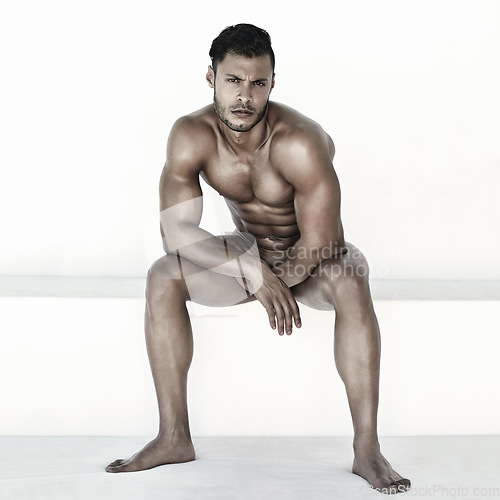 Image of Nude, body and man in portrait isolated on a wall background for health, fitness and wellness. Naked, strong and face of a sexy male model sitting with muscles for power, sports and exercise results