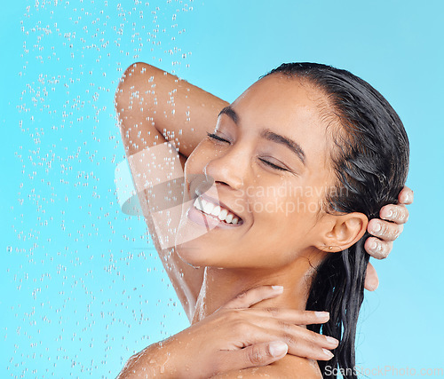 Image of Skincare, shower and woman in studio for hair, water splash and cleaning against a blue background. Face, relax and girl model happy, beauty and splash, hygiene routine while washing and isolated