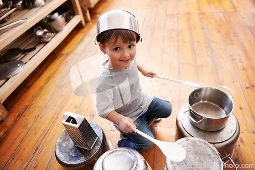 Image of Portrait, fun and boy child playing drums on pans on a floor, happy and enjoying music. Face, creative and kid with pots for musical entertainment, silly and carefree in a kitchen on the weekend