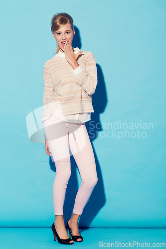 Image of Portrait, wow and hand on mouth with a woman in studio on a blue background for surprise or shock. Fashion, gasp and hand gesture with an attractive young female model standing against a wall