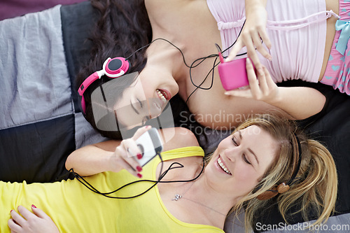 Image of Music, friends and relax on a bed from above while listening to track on mp3 player together. Retro, audio and gen z girls bonding, talking and laughing in a bedroom on the weekend with vintage tech