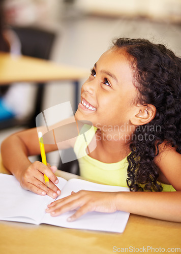 Image of Happy, school and child writing in her book while listening to a lesson in the classroom. Happiness, smile and young girl kid student doing an education activity, studying or homework by her desk.