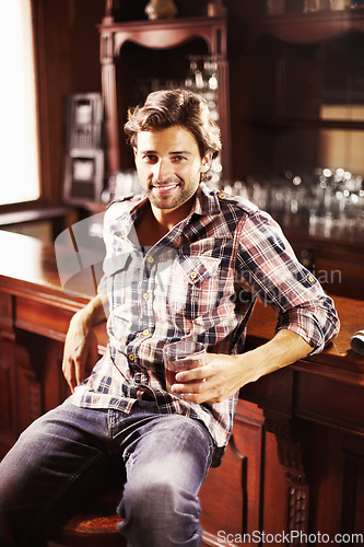 Image of Portrait, smile and man with whiskey in pub sitting by counter alone. Alcohol, happiness and male person in bar for drinking liquor, beverage or drink in tavern, relaxing and enjoying time alone.