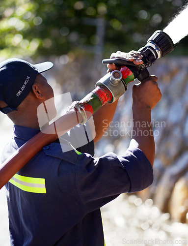 Image of Firefighter man, water and spraying hose for emergency, rescue or firefighting services in the outdoors. Fireman using big liquid pressure pipe to spray down or put out fire outside for safety