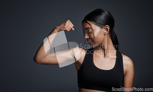 Image of Sports, smile and woman flexing bicep in studio isolated on black background. Strong, happy and Indian female athlete with muscle, arm strength and bodybuilder ready for fitness, workout or exercise.