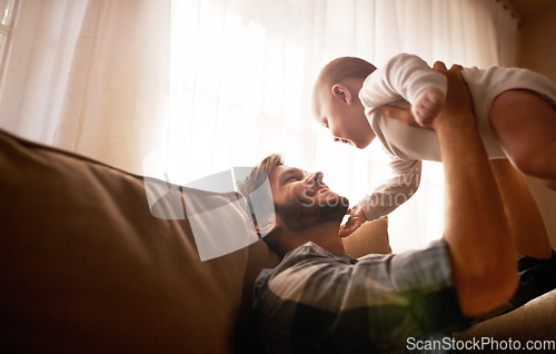 Image of Funny, dad and lifting baby on sofa in home living room, playing or bonding together. Happy, care and father holding infant, newborn or child on couch in lounge, having fun and enjoying quality time.