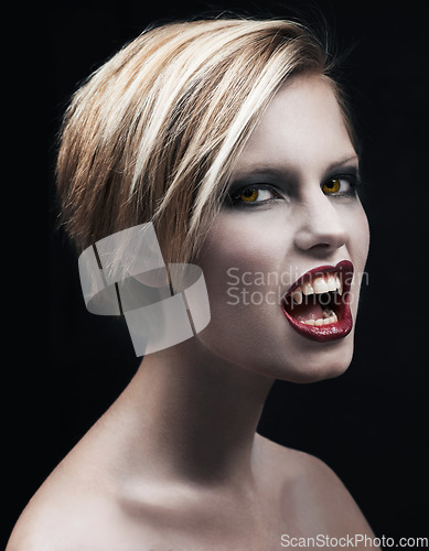 Image of Portrait, fangs and a woman vampire in studio on a dark background for halloween or cosplay. Fantasy, horror and scary with an attractive young monster posing as an evil or supernatural creature