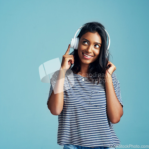 Image of Woman, thinking and headphones with music in studio with happiness and web audio. Blue background, Indian female person and young model listening, hearing and streaming a song with smile and mockup