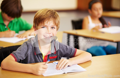 Image of Portrait, education and learning with a student boy sitting by his desk in a classroom for child development. School, kids and writing with a happy young male child in class to study using a notebook