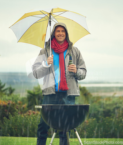 Image of Happy man, umbrella and barbecue in rain with beer for meal, supper or dinner on the fire grill. Male person smiling for insurance, cover or protection while cooking under raining or stormy weather