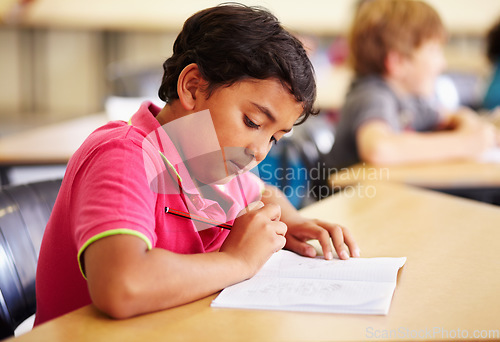 Image of Education, student and boy in a classroom, writing and studying for a test, exam and notebook. Male child, school and kid with a book, pencil and creative with development, growth and learning