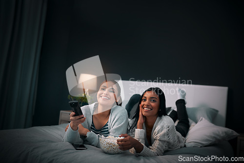 Image of Women friends on bed at night for movies, eating popcorn and happy sleepover at home with streaming service or television. Gen z people relax in bedroom with TV film, cinema subscription and internet