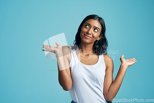 Image of Comparison, thinking and woman with a choice in a studio with a question, idea or dream. Decision, doubt and Indian female model with option or shrug hand sign by blue background with mockup.