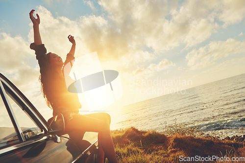 Image of Road trip, sunset and arms raised with a woman at the coast, sitting on her car bonnet during travel for freedom or escape. Nature, flare and water with a young female tourist traveling in summer