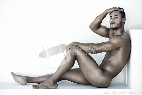 Image of Portrait, nude and a sexy man sitting on the floor of a studio against a white background for natural body care. Fitness, skin and wellness with a handsome young male model posing naked for health