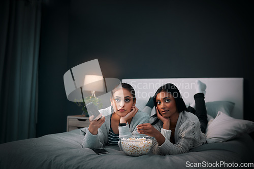 Image of Girls night, young women and popcorn while watching television on a bed in bedroom. Relaxing or entertainment, fun and female friends with snack with streaming movie or series together at home